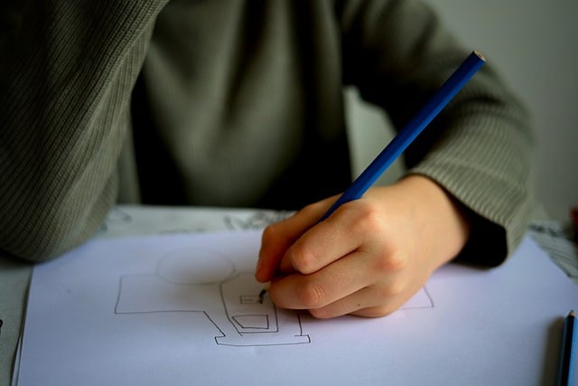 A stock image of a young person's hand holding a blue pencil. They are drawing a picture. We cannot see their face.
