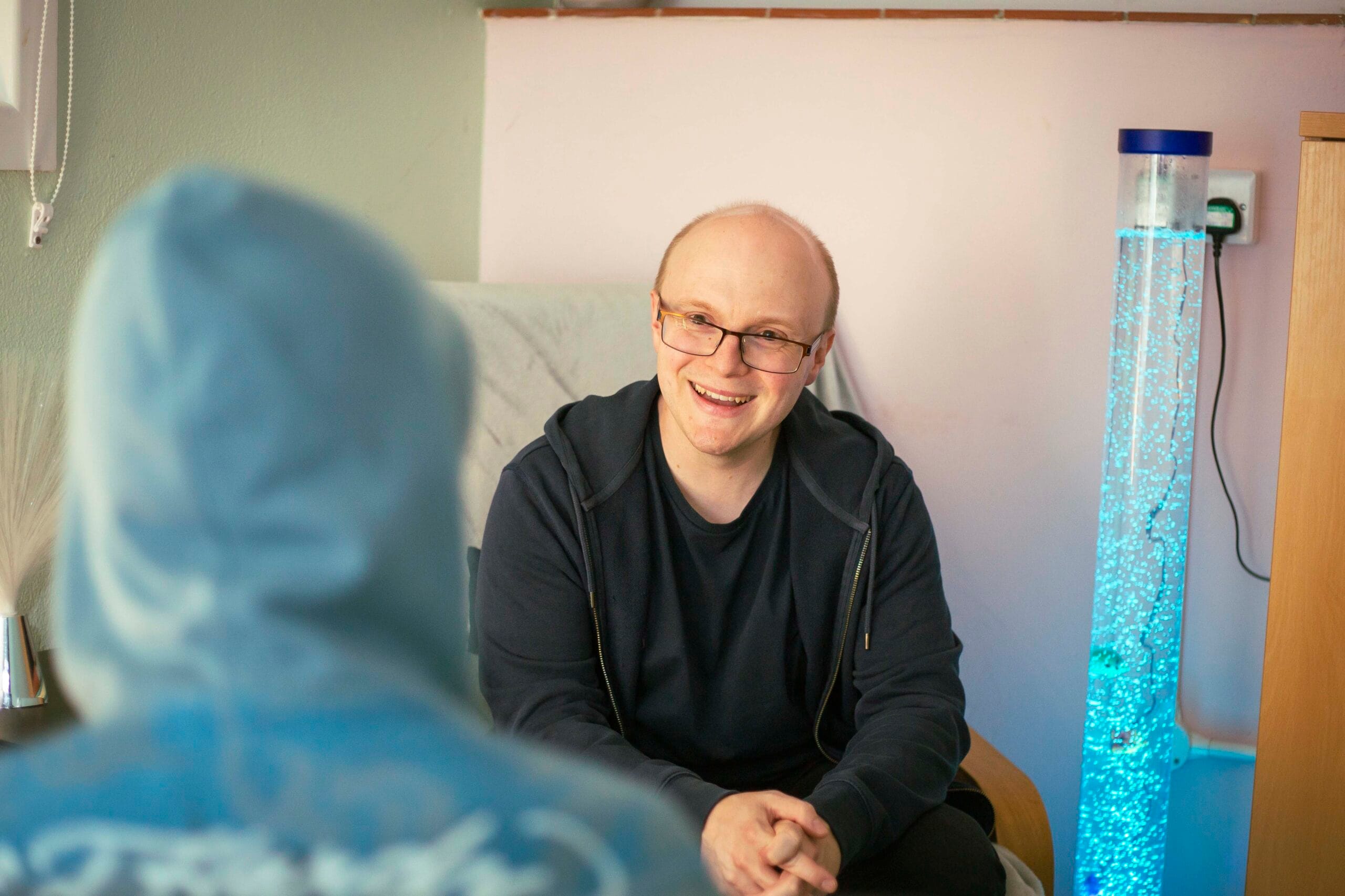 Image shows Roy Peach coaching a person. Roy is in the background, facing the camera's direction. The back of the person he is coaching is in the foreground. The client has a hoodie hood up. Roy is smiling.